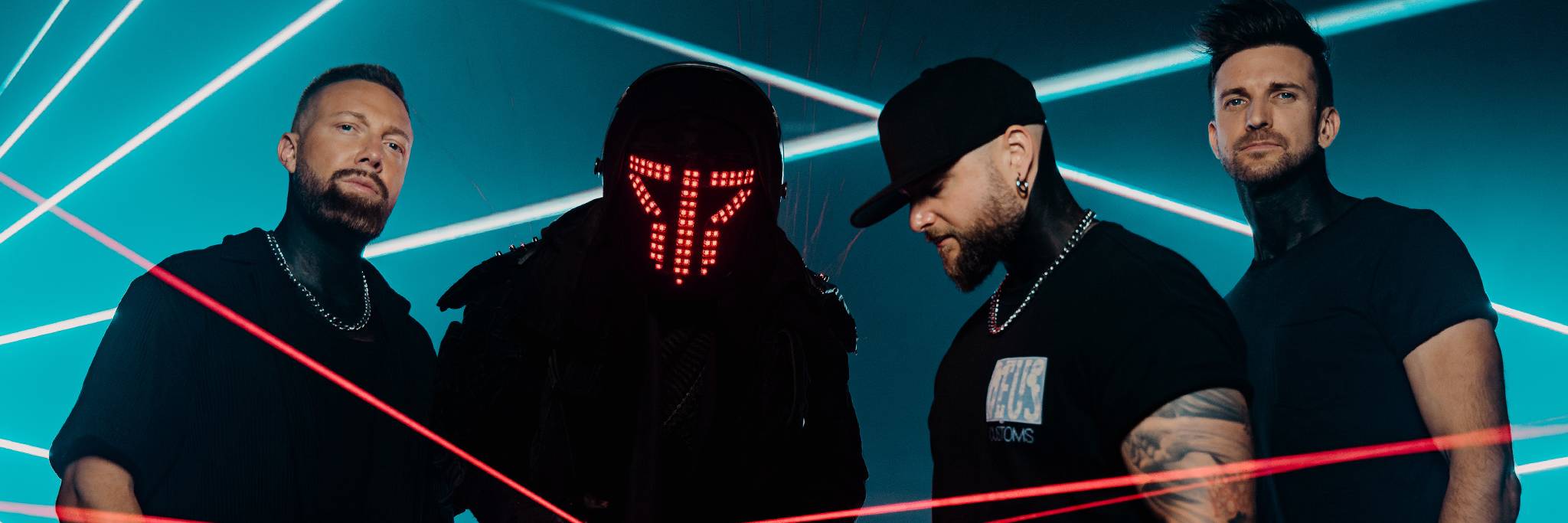 Fyra män står mitt bland röda laserstrålar och blått ljus; en bär en futuristisk hjälm med röda LED-lampor, medan de andra bär svarta skjortor och hattar.