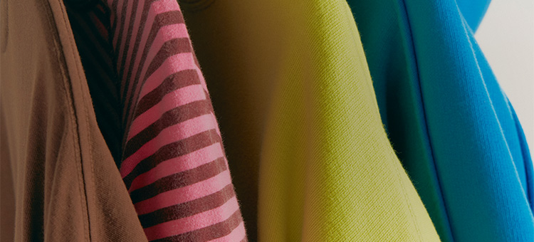 Close-up of colorful fabric garments including brown, pink striped, yellow-green, teal, and blue textiles arranged together.