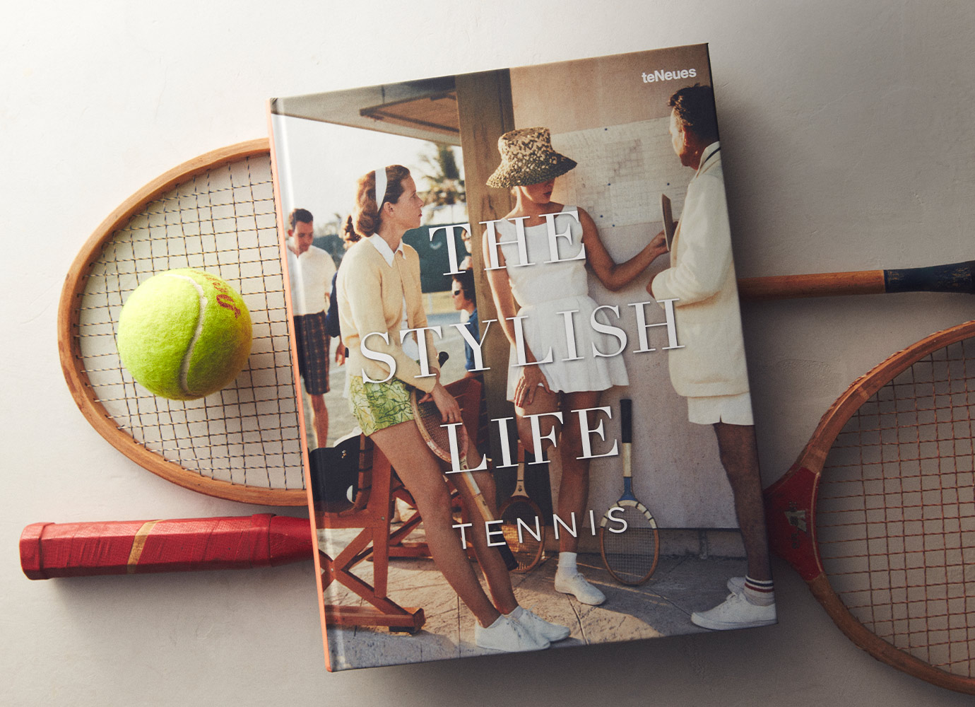 Coffee table book titled 'The Stylish Life Tennis' displayed with vintage wooden tennis racquets and a tennis ball.