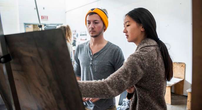 Picture of an art professor giving advice to her student in front of a painting. 