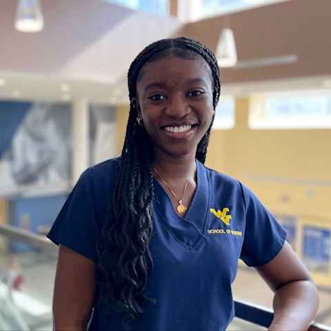 Selasi Asamoah wears dark blue scrubs with a gold Flying WV School of Nursing logo.
