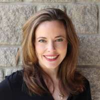 Smiling woman standing in Stewart Hall. She has long dark hair and wears a black suit jacket. 