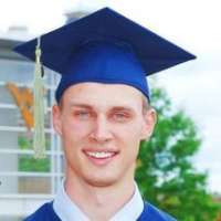 Smiling man wearing a dark blue graduation cap and gown.,