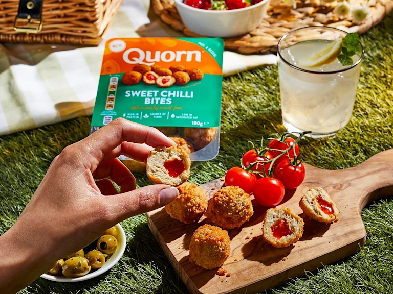 Quorn Sweet Chilli Bites served on a wooden board with fresh tomatoes and olives at a picnic setting