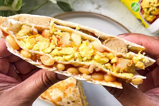 Vegetarian scrambled egg, sausage, beans and potato waffles folded into a wrap with plants in the background.