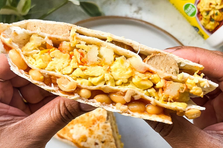 Vegan scrambled egg, sausage, beans and potato waffles folded into a wrap with plants in the background.
