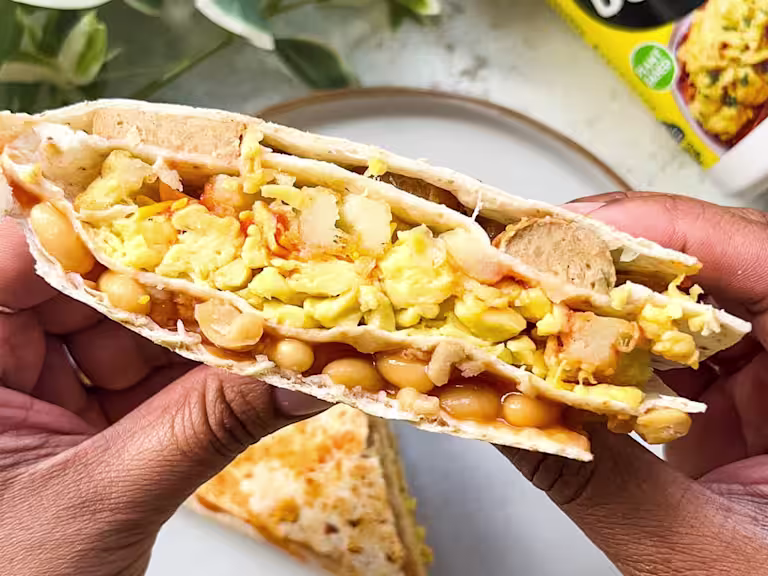 Vegan scrambled egg, sausage, beans and potato waffles folded into a wrap with plants in the background.