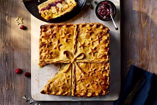 Quorn Roast Festive Pie with slice cut served on the side alongside a red sauce.