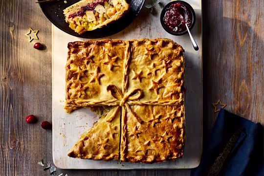 Quorn Roast Festive Pie with  slice cut served on the side alongside a red sauce.