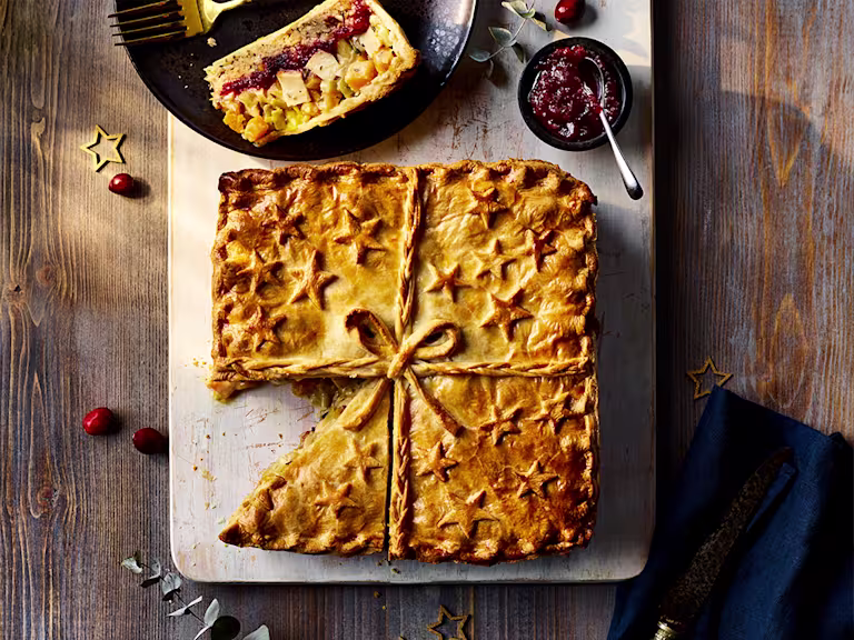 Quorn Roast Festive Pie with slice cut served on the side alongside a red sauce.