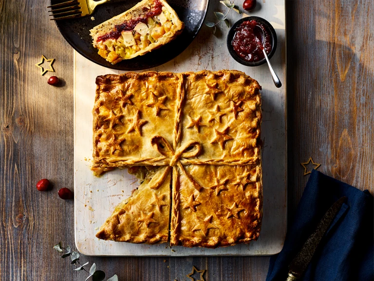 Quorn Roast Festive Pie with  slice cut served on the side alongside a red sauce.