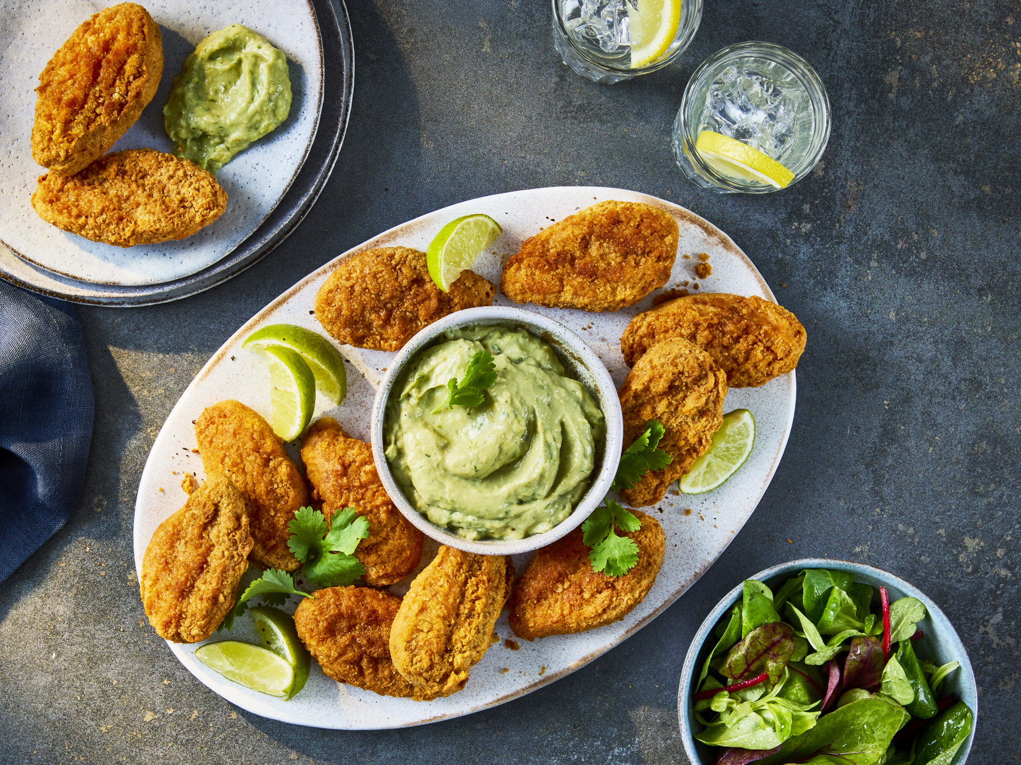 Crispy Quorn Hot & Spicy Bites served on a platter with a bowl of creamy avocado dip, lime wedges, and a side salad.