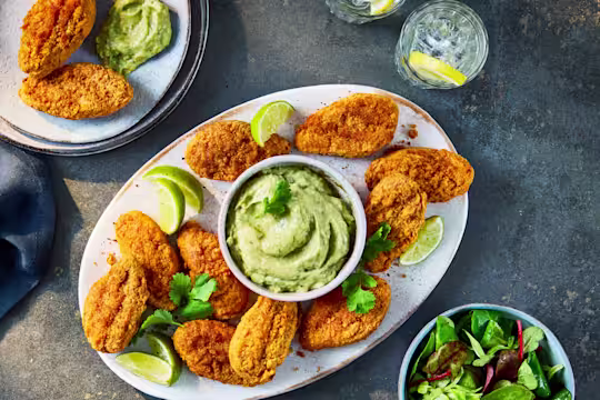 Crispy Quorn Hot & Spicy Bites served on a platter with a bowl of creamy avocado dip, lime wedges, and a side salad.