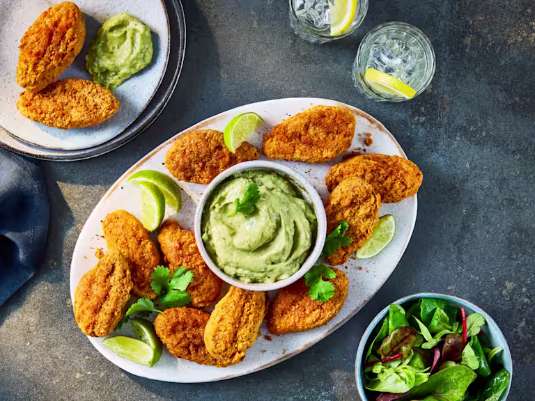 Crispy Quorn Hot & Spicy Bites served on a platter with a bowl of creamy avocado dip, lime wedges, and a side salad.