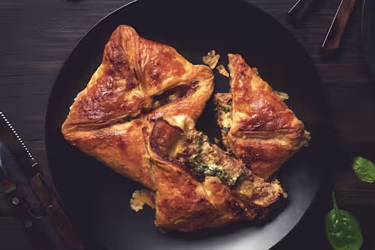 Two puff pastry steak parcels arranged on a black plate with one halved to show a filling of Quorn Steak Strips, spinach, and cheese.
