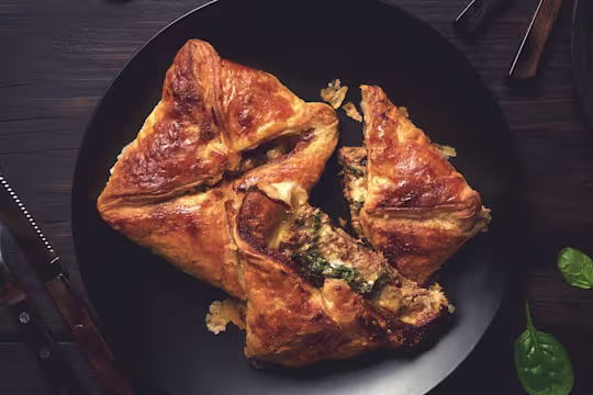 Two puff pastry steak parcels arranged on a black plate with one halved to show a filling of Quorn Steak Strips, spinach, and cheese.