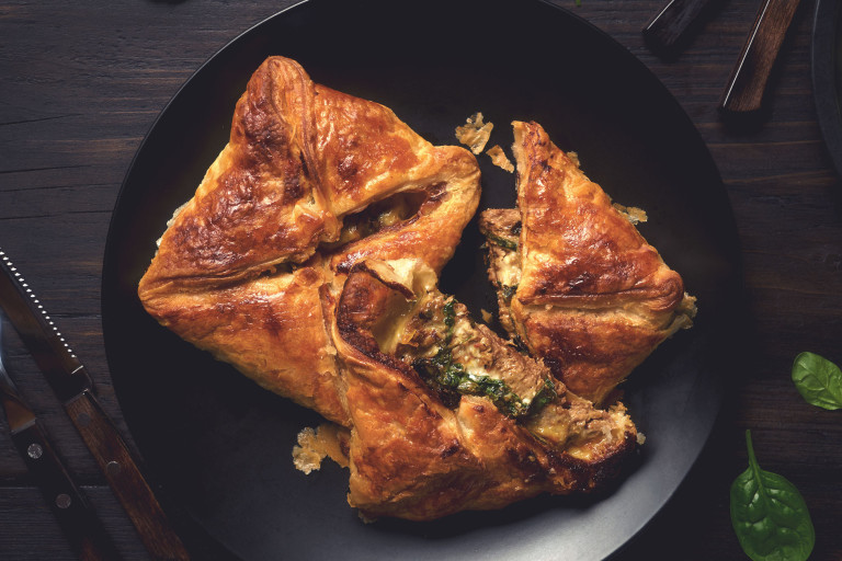 Two puff pastry steak parcels arranged on a black plate with one halved to show a filling of Quorn Steak Strips, spinach, and cheese.