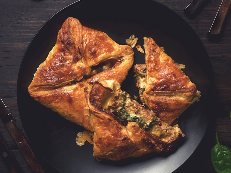 Two puff pastry steak parcels arranged on a black plate with one halved to show a filling of Quorn Steak Strips, spinach, and cheese.