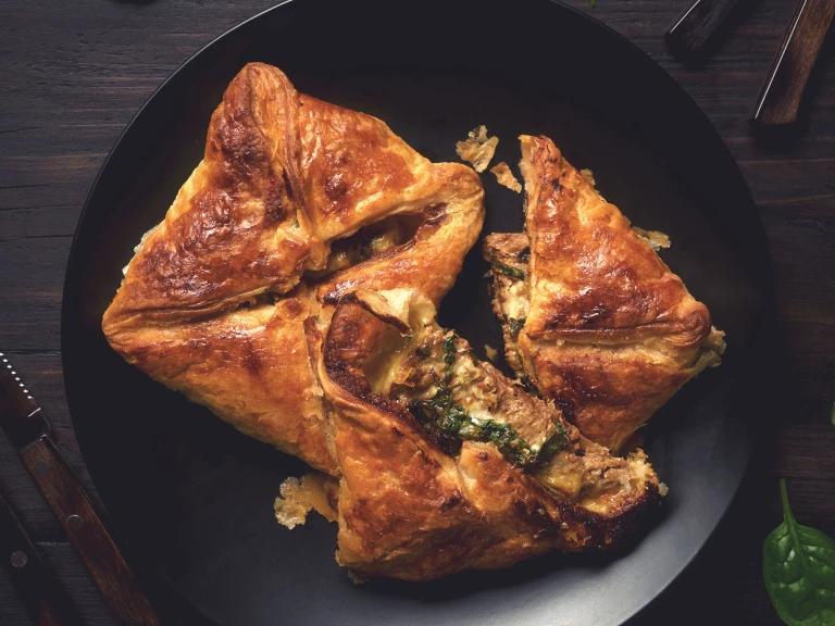 Two puff pastry steak parcels arranged on a black plate with one halved to show a filling of Quorn Steak Strips, spinach, and cheese.