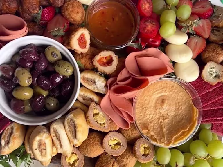 Quorn Cocktail Sausages, Picnic Eggs, Mini Sausage Rolls, Vegan Smoky Ham Free Slices, Garlic and Herb Bites, Sweet Chilli Bites and Garlic and Herb Bites on a board with olives, hummus, strawberries, grapes, cheese and beetroot crackers.