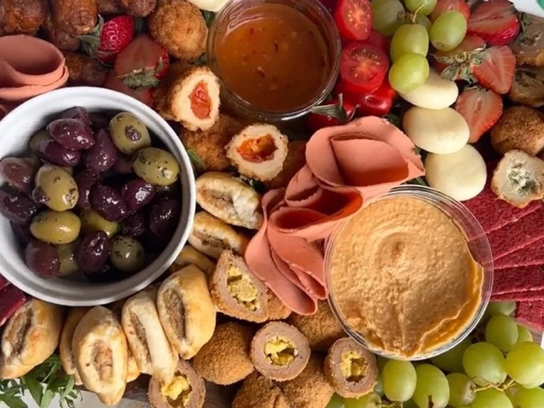 Quorn Cocktail Sausages, Picnic Eggs, Mini Sausage Rolls, Vegan Smoky Ham Free Slices, Garlic and Herb Bites, Sweet Chilli Bites and Garlic and Herb Bites on a board with olives, hummus, strawberries, grapes, cheese and beetroot crackers.