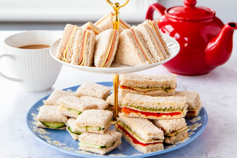 Sandwiches served on a platter with a pot of tea in the back.