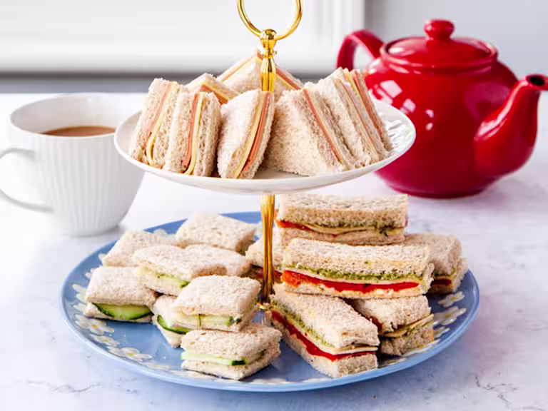 Sandwiches served on a platter with a pot of tea in the back.