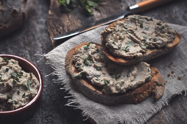 A pate made of mushrooms and Quorn Pieces spread on two pieces of rustic white bread.