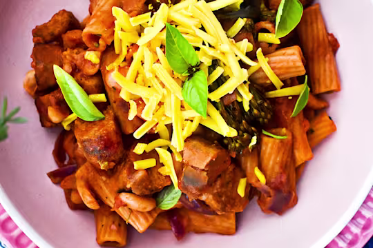 Vegan one-pot pasta with sausage and broccoli topped with cheese and herbs served in a pink bowl.