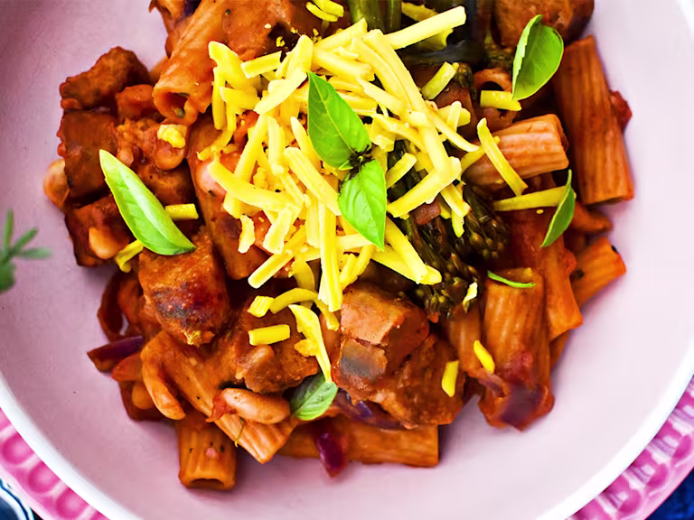 Vegan one-pot pasta with sausage and broccoli topped with cheese and herbs served in a pink bowl.