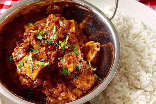 Tomato Quorn Beef Roast Curry served in a metal dish and topped with coriander with a side of boiled rice.