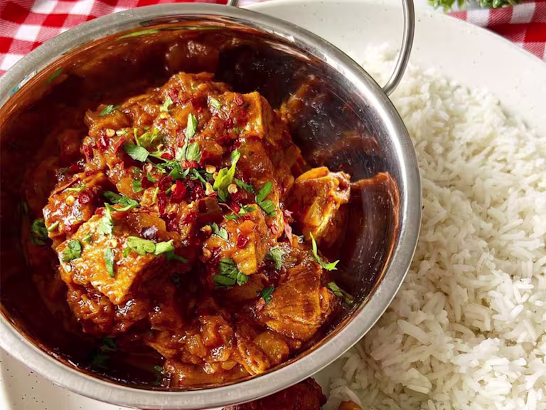 Tomato Quorn Beef Roast Curry served in a metal dish and topped with coriander with a side of boiled rice.