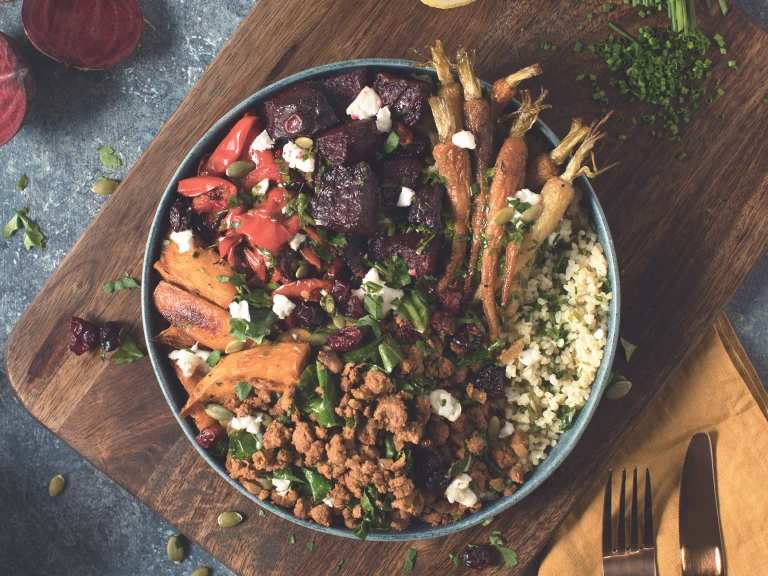 A bowl of bulgur wheat topped with Quorn Grounds, roasted carrots, roasted beets, sweet potato, and bell pepper topped with green onions, dried cranberries, and pumpkin seeds.