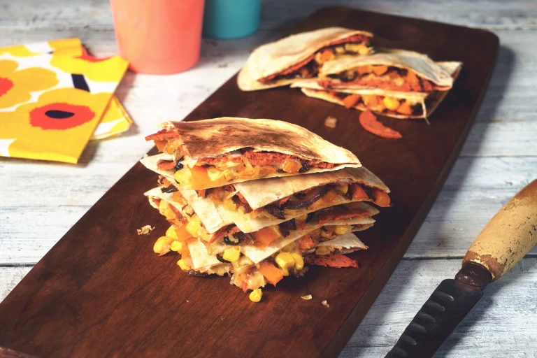 Vegan quesadilla made with Quorn Vegan Pepperoni slices in tortilla wraps, stacked on top of each other on a wooden board