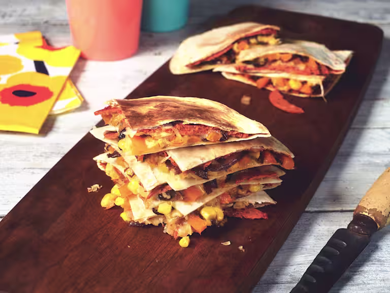 Vegan quesadilla made with Quorn Vegan Pepperoni slices in tortilla wraps, stacked on top of each other on a wooden board