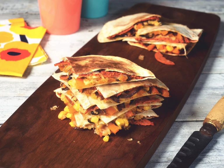 Vegan quesadilla made with Quorn Vegan Pepperoni slices in tortilla wraps, stacked on top of each other on a wooden board