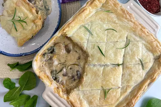 Creamy sausage spinach and mushroom pie garnished with herbs in a dish with a scoop taken out and served on a plate.