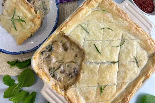 Creamy sausage spinach and mushroom pie garnished with herbs in a dish with a scoop taken out and served on a plate.