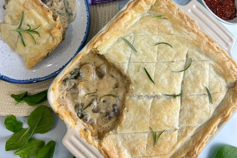 Creamy sausage spinach and mushroom pie garnished with herbs in a dish with a scoop taken out and served on a plate. 