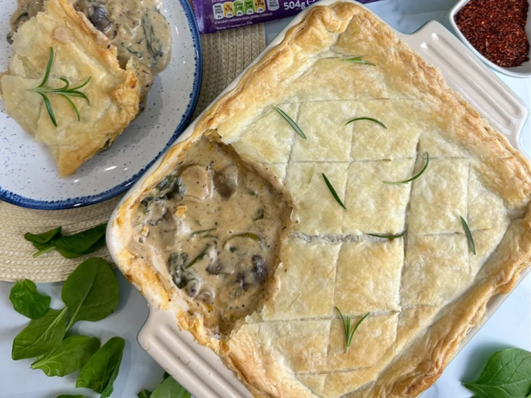 Creamy sausage spinach and mushroom pie garnished with herbs in a dish with a scoop taken out and served on a plate. 