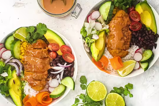 Two poke bowls served in white bowls with sauce on the sides and sliced limes.