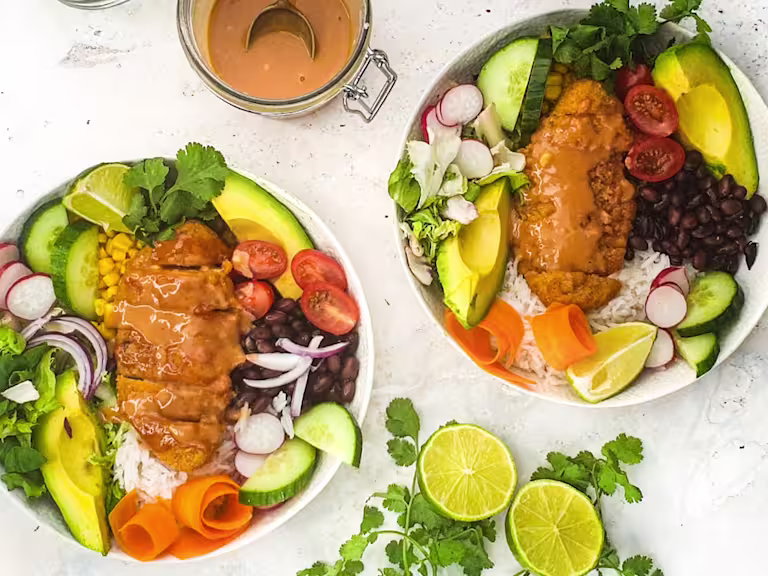 Two poke bowls served in white bowls with sauce on the sides and sliced limes.