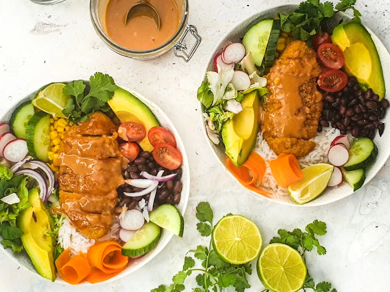 Two poke bowls served in white bowls with sauce on the sides and sliced limes.