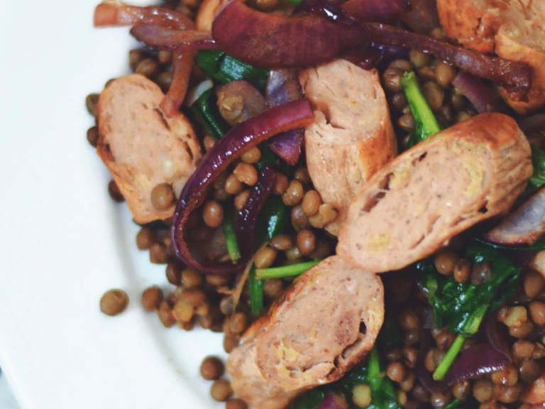 Lentils topped with caramelised red onions, spinach, and Quorn Sausages on a white plate.