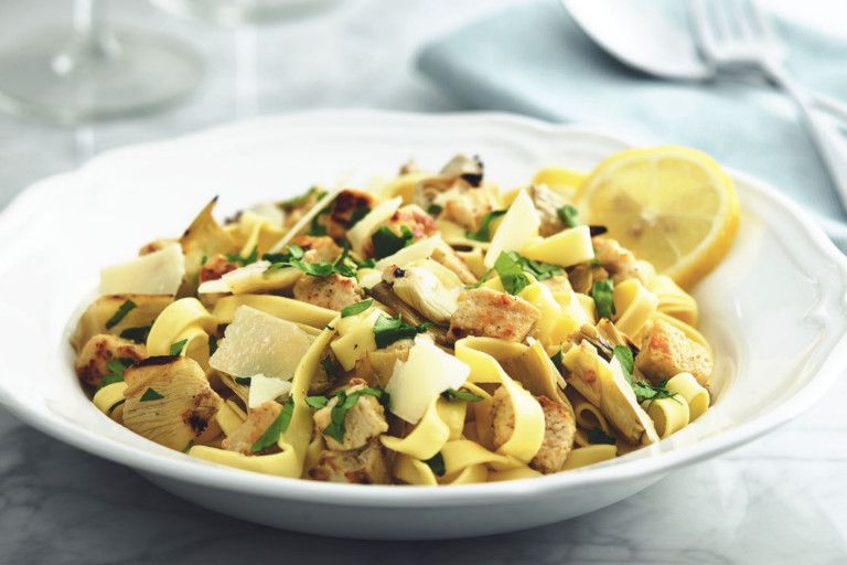 Tagliatelle pasta with Quorn Pieces and artichokes topped with cheese and parsley with a lemon wedge on the side.