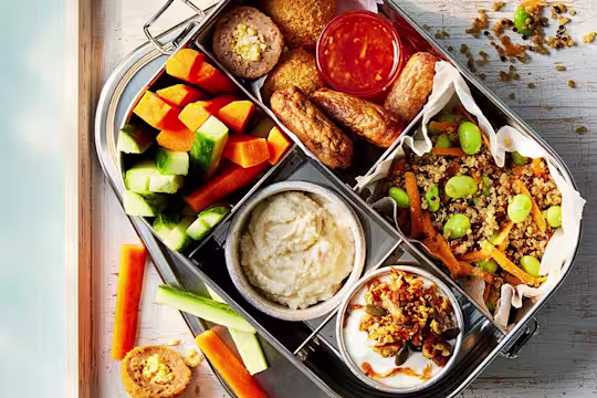 Vegetarian high-protein bento box with Quorn Cocktail Sausages, vegetarian picnic eggs, quinoa salad, hummus, raw vegetable sticks, and carrot granola yoghurt