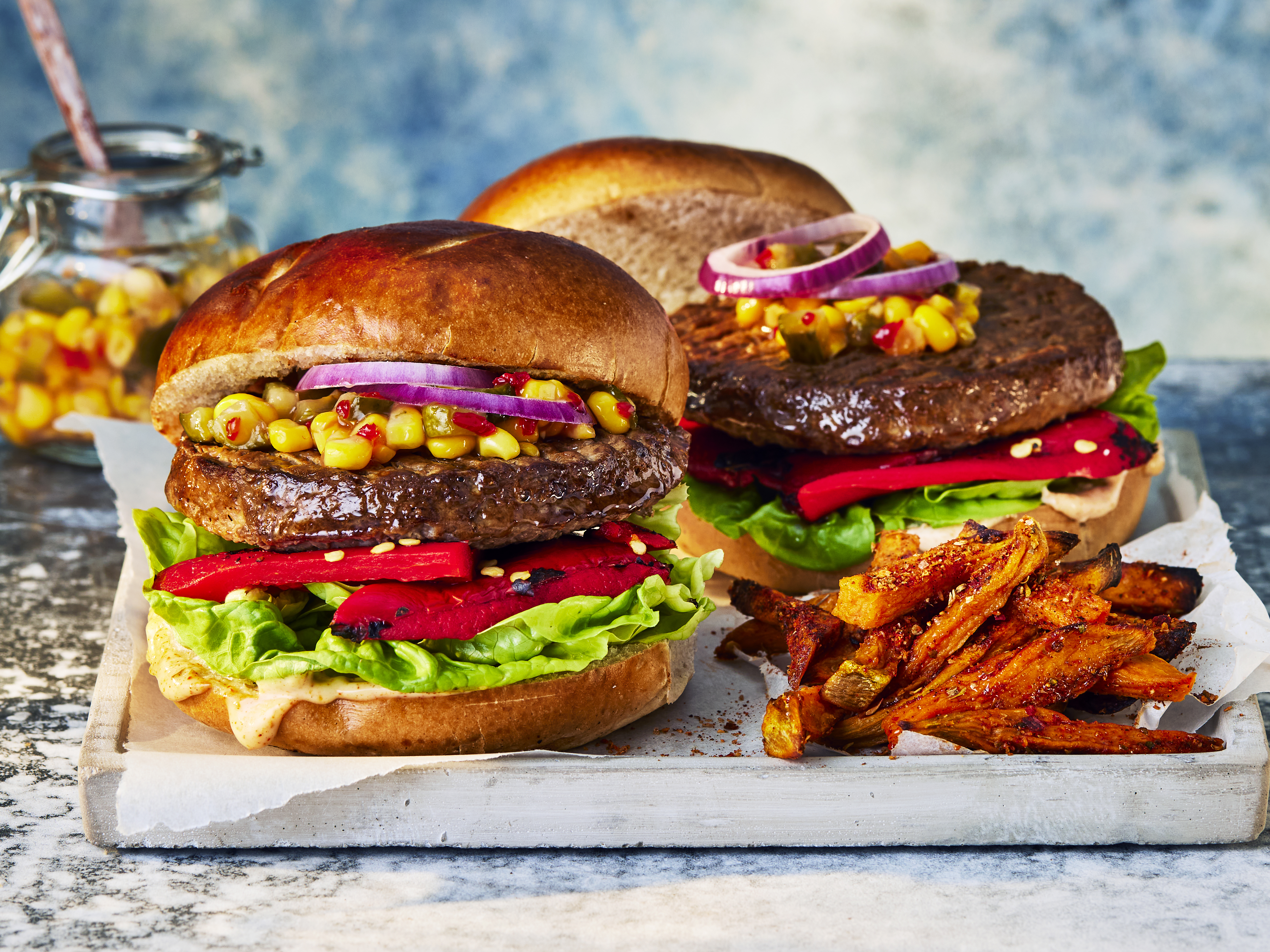 A Quorn Quarter Pounder piled high with burger sauce, greens, tomato slices, gherkins, radishes, red onion, and avocado.
