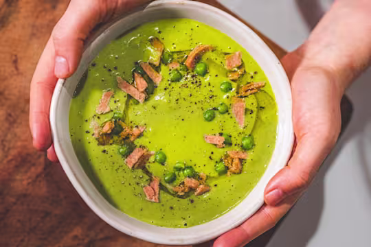 Vegan Pea And Ham soup served in a white bowl with ham trimmings on the top.