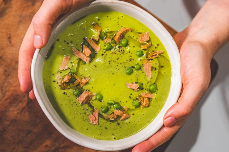 Vegan Pea And Ham soup served in a white bowl with ham trimmings on the top.