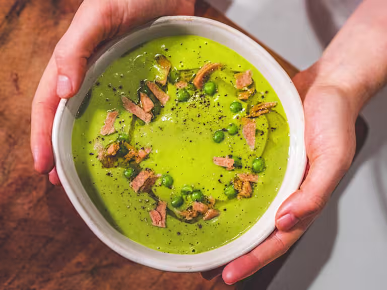 Pea And Ham soup served in a white bowl with ham trimmings on the top.